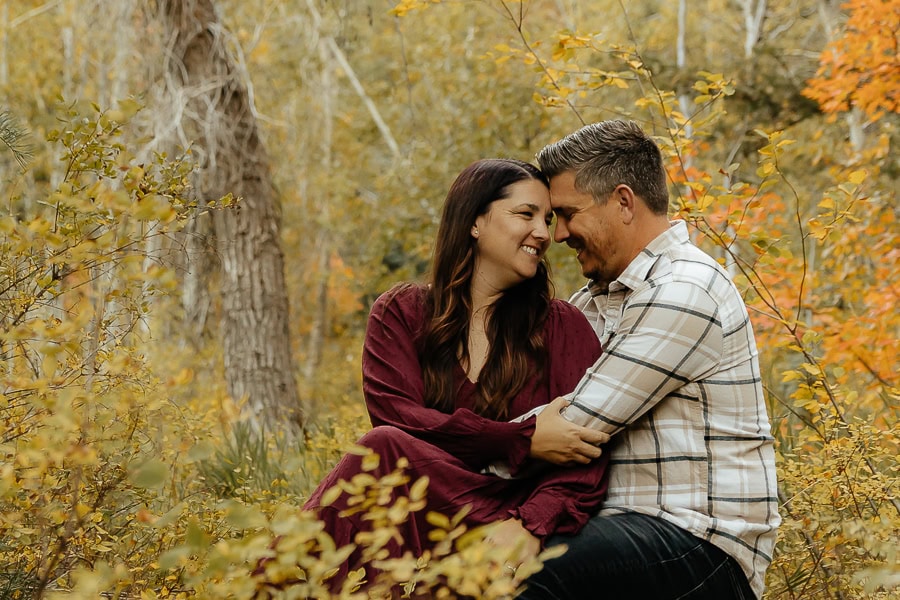 Mountain engagement photos in the Utah mountain forests. Woman in red dress and man in brown plaid sitting together.